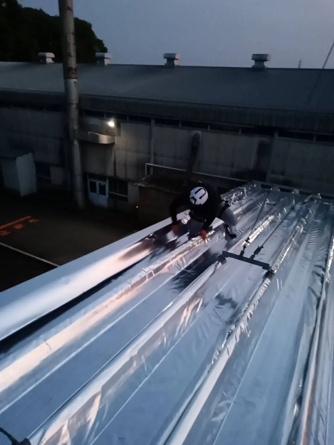 工場の折半屋根への特殊シート施工作業風景